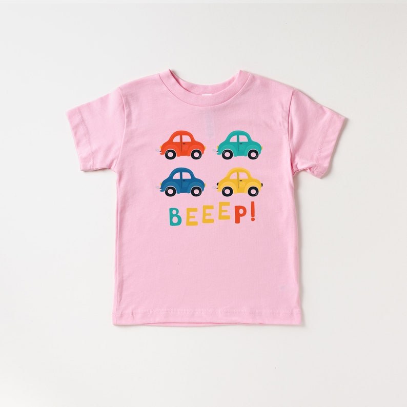 May include: Pink short-sleeved t-shirt with a graphic of four colourful toy cars and the text "BEEEP!" printed on the front.