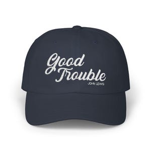 Puede incluir: Gorra de béisbol azul marino con la frase "Good Trouble" en escritura blanca. El texto "JOHN LEWIS" está debajo. La gorra tiene una visera curva y un diseño clásico de seis paneles.