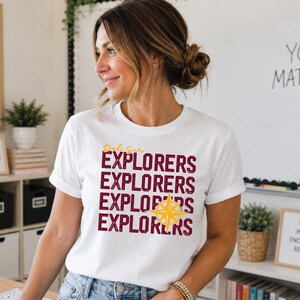 Puede incluir: Una camiseta blanca de manga corta con el texto "Del Sur" en letra cursiva amarilla y la palabra "EXPLORERS" impresa cuatro veces en una fuente de color rojo oscuro desgastado. Un gráfico de rosa de los vientos amarilla cubre la tercera línea.