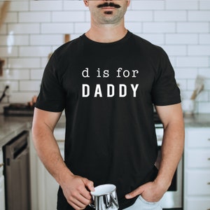May include: Black t-shirt with white text that reads "d is for DADDY".