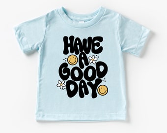 May include: Light blue short-sleeved t-shirt with a black graphic that says "HAVE A GOOD DAY" with smiley faces and flowers.
