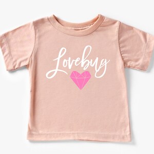 May include: A light pink t-shirt with the text "Lovebug" in white script and a pink diamond-shaped heart.