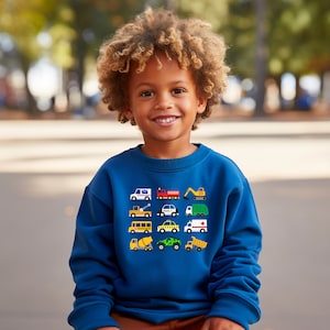 May include: A young boy wearing a blue sweatshirt with a colourful pattern of various vehicles on the front. The vehicles include a school bus, a police car, a fire engine, a tow truck, a construction truck, and a delivery truck.