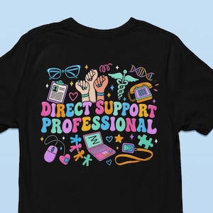 May include: A black t-shirt featuring a small front graphic with the letters DSP above a pink heart containing a blue puzzle piece. The back displays the text DIRECT SUPPORT PROFESSIONAL in colourful letters surrounded by icons of hands, a laptop, and medical symbols.