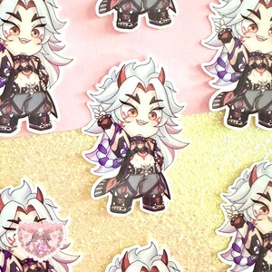 May include: A sticker featuring a cartoon character with white hair, red eyes, and a mischievous grin. The character is wearing a black and purple outfit with a red heart on the chest. The sticker is on a pink and gold glitter background.