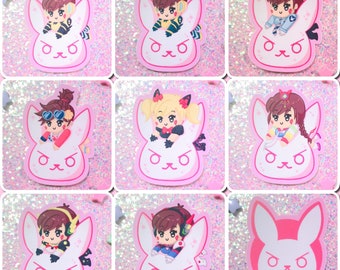 May include: Nine pink and white bunny stickers featuring different Overwatch characters. Each sticker has a white bunny face with pink ears and a pink nose. The characters are all female and are wearing different outfits. The stickers are perfect for adding a touch of fun to your laptop, water bottle, or phone.