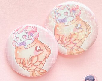 May include: Two round, white, button pins with a pink background. Each pin features a white cat wearing a blue bow tie inside a pink and orange taiyaki fish.