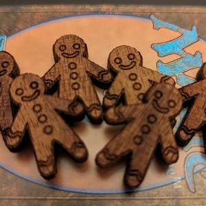 May include: Six wooden gingerbread man cutouts with smiling faces and button details. The gingerbread men are a warm brown color and are arranged on a decorative surface.