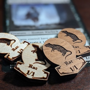 May include: Four wooden game pieces with a rat design and the text "Rat 1/1" on each piece. The pieces are used for a board game or role-playing game.