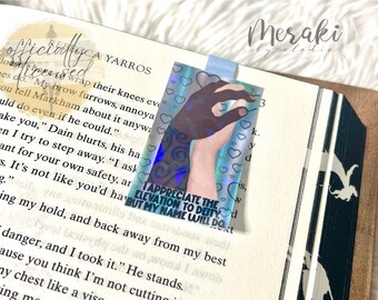 May include: A holographic bookmark with a blue and green background. The bookmark features a hand with a dark skin tone making a fist with the thumb and index finger touching. The bookmark has a white border with a white heart pattern. The text on the bookmark reads "I appreciate the elevation to deity but my name will do."
