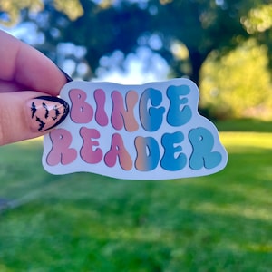 May include: A sticker with the words "Binge Reader" in a colorful, retro font. The letters are pink, orange, yellow, and blue.