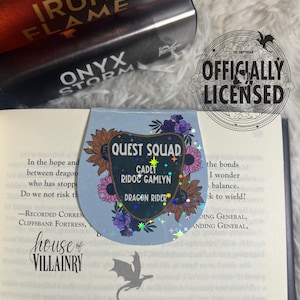May include: A holographic bookmark featuring a dragon rider with the text "Quest Squad, Cadet Ridoc Gamlyn, Dragon Rider". The bookmark is decorated with flowers and stars.