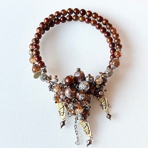 May include: A brown beaded necklace with a large cluster of brown, gold, and silver beads hanging from the bottom.