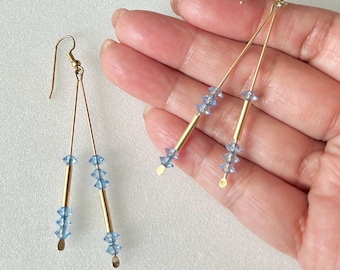 May include: A pair of gold dangle earrings with light blue crystal beads. The earrings have a simple design with two gold wires and a cluster of beads at the bottom.