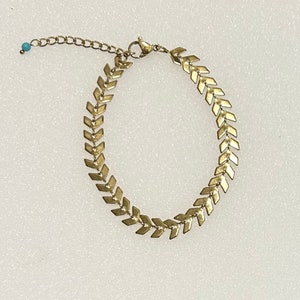 Puede incluir: Un brazalete de cadena dorada con un patrón de chevron. El brazalete está hecho de metal y tiene un cierre de langosta.