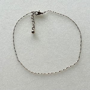 May include: A silver chain anklet with a small ball at the end of the clasp.
