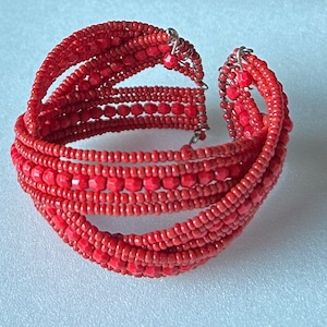 May include: A red beaded bracelet with multiple strands of beads woven together. The bracelet has a silver clasp.
