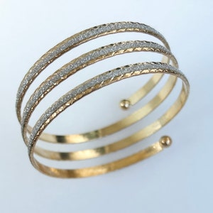 Op de afbeelding: Drievoudige armband in goudkleur met een glinsterende zilveren afwerking.