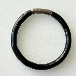 Puede incluir: Un brazalete negro con una banda plateada.