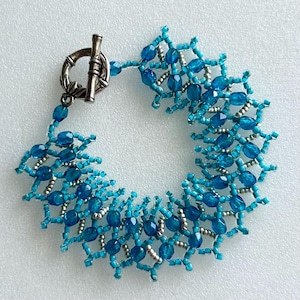 May include: A turquoise and silver beaded bracelet with a silver toggle clasp. The bracelet is made with small, round beads and has a delicate, intricate design.