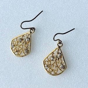 May include: A pair of gold filigree earrings with small clear rhinestones. The earrings are teardrop shaped and have a delicate design.