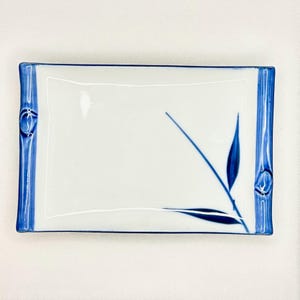 May include: A rectangular white ceramic serving tray featuring a blue painted bamboo stalk design on the left and right edges. The center of the tray displays a single blue painted bamboo branch with two leaves extending diagonally across the surface.