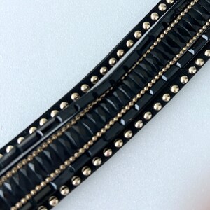 May include: Black leather trim with silver studs and a row of black rectangular beads with a gold chain running through them.