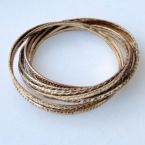 May include: A set of gold-toned bangle bracelets with intricate etched designs. The bracelets are stacked on top of each other.