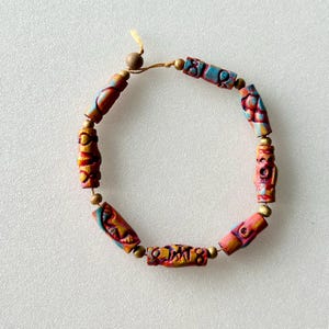 May include: A colourful bracelet made of wooden beads with intricate carvings and painted designs in shades of red, orange, blue, and gold.
