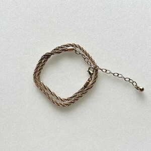 May include: A gold-toned chain bracelet with a delicate, twisted design. The bracelet has a lobster clasp and an extender chain with a small ball at the end.