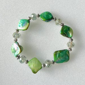 Puede incluir: Un brazalete de cuentas de concha verde e iridiscente con cuentas espaciadoras plateadas.