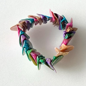 May include: A colorful bracelet made of iridescent, multi-colored, shell-like pieces. The bracelet is made of many small, triangular pieces that are arranged in a circle.