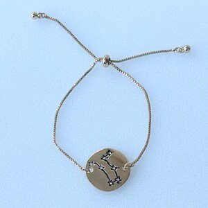May include: A gold adjustable bracelet with a round charm featuring the Gemini constellation with small clear rhinestones.