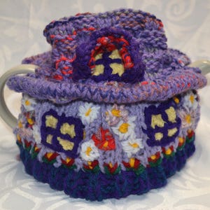 May include: A whimsical, hand-crocheted tea cozy in shades of purple, blue, red, and yellow. The cozy is designed to resemble a fairy house, complete with windows and a roof. The cozy is designed to fit a standard size teapot.