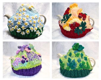 Può includere: Quattro teiere in ceramica, ognuna coperta da un copriteiera lavorato a maglia a mano. I disegni includono un campo di margherite bianche su sfondo blu, una base rossa con fiori gialli e verdi, una base viola con fiori e una base verde.