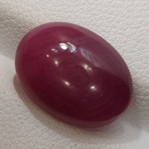 May include: A deep red oval-shaped gemstone with a smooth, polished surface.