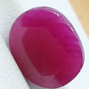 May include: A vibrant, deep pink oval-shaped gemstone with a smooth, polished surface.
