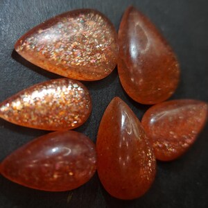 May include: Six teardrop-shaped sunstone cabochons in shades of orange and red with a glittery, iridescent finish.