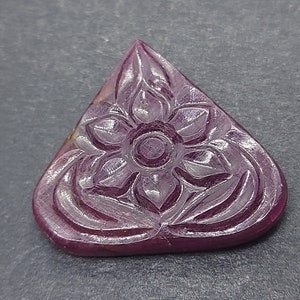May include: A carved pink gemstone pendant in the shape of a triangle with a floral design.