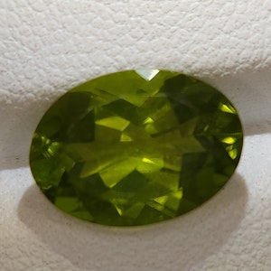 Peut inclure: Une pierre pr&eacute;cieuse ovale de couleur verte avec une taille facet&eacute;e. La pierre pr&eacute;cieuse est plac&eacute;e sur un fond blanc.