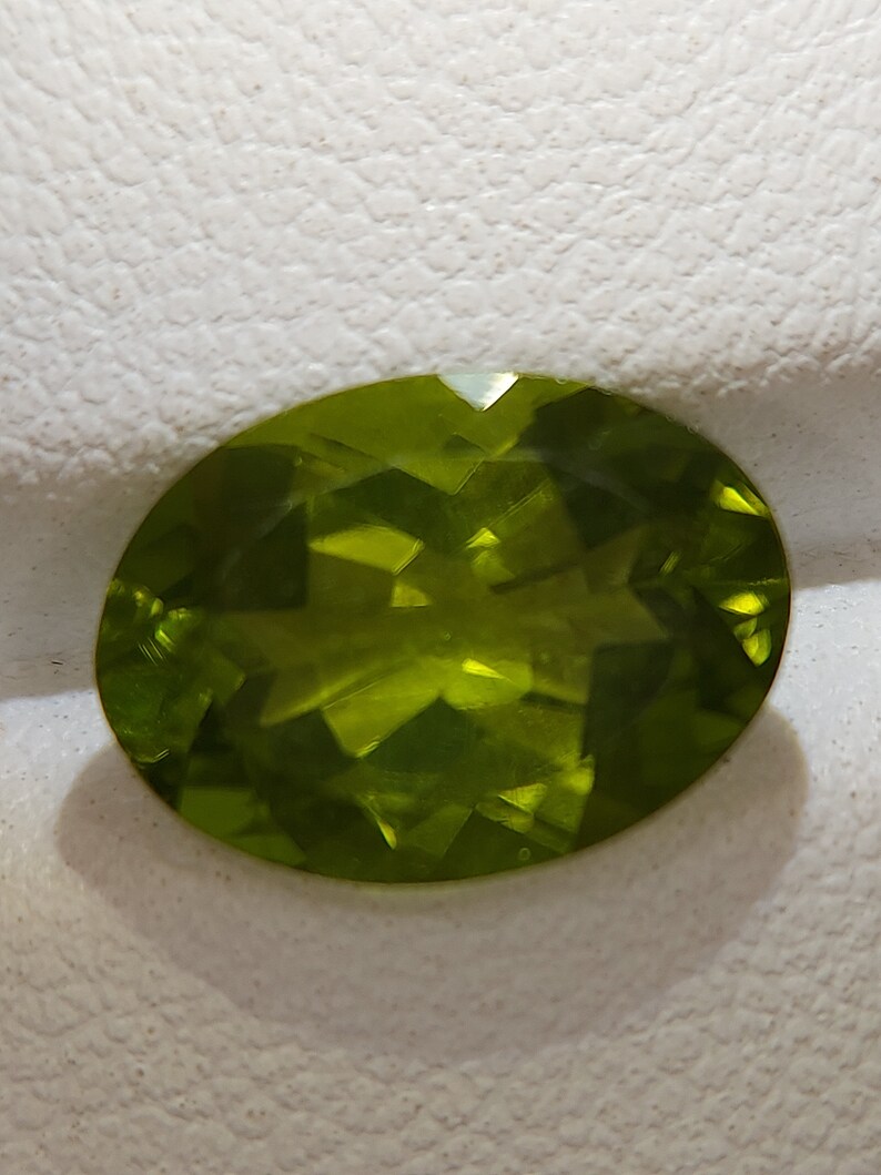 Peut inclure: Une pierre pr&eacute;cieuse ovale de couleur verte avec une taille facet&eacute;e. La pierre pr&eacute;cieuse est plac&eacute;e sur un fond blanc.
