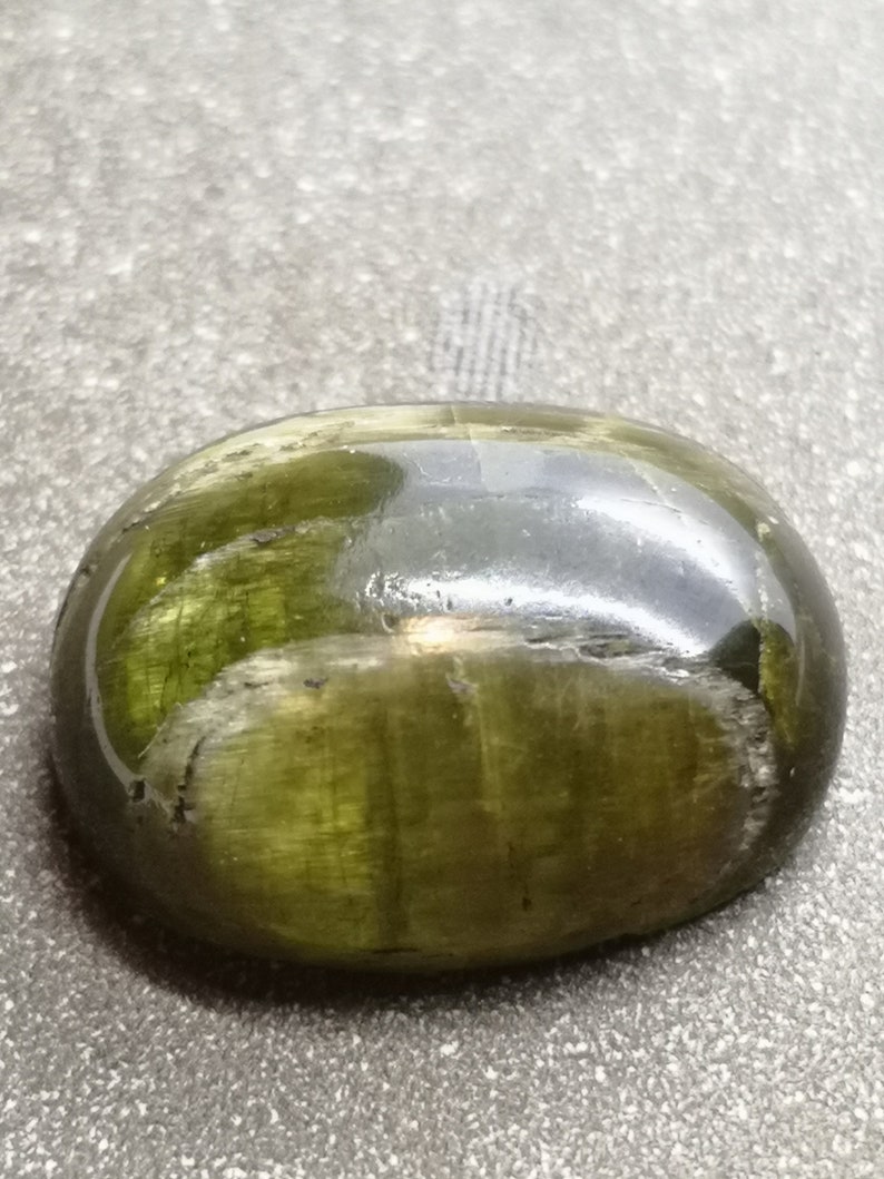 May include: A smooth, oval-shaped green gemstone with a dark green, almost black, center. The stone has a glossy finish and appears to be translucent.