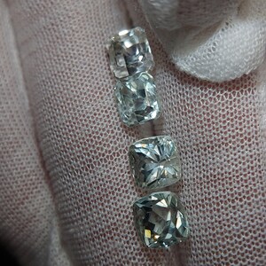 May include: Four square-shaped gemstones, two are clear and two are light blue, arranged vertically in a row.