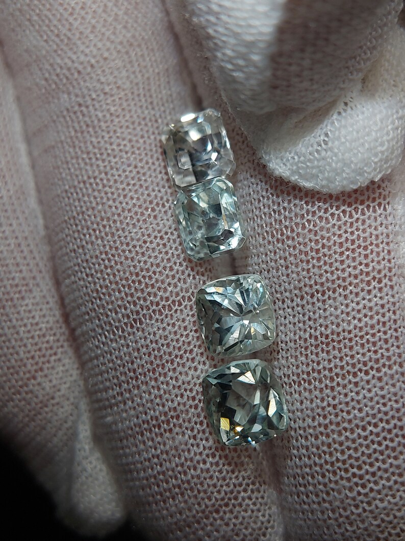 May include: Four square-shaped gemstones, two are clear and two are light blue, arranged vertically in a row.
