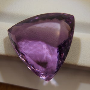 May include: A large, triangular, purple amethyst gemstone with a faceted cut.