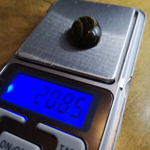 May include: A digital scale with a green and black gemstone on the weighing platform. The scale reads "2.06g".