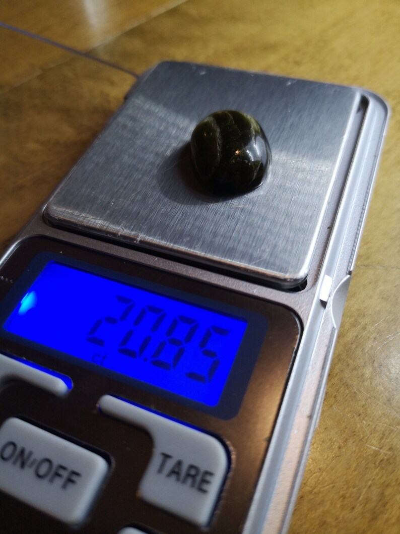 May include: A digital scale with a green and black gemstone on the weighing platform. The scale reads "2.06g".