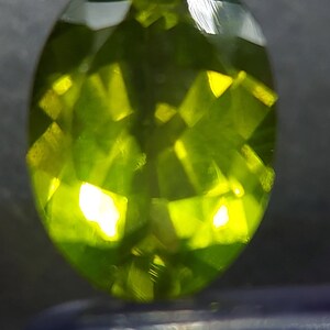 Peut inclure: Une pierre pr&eacute;cieuse ovale de couleur vert vif avec une taille facet&eacute;e. La pierre pr&eacute;cieuse r&eacute;fl&eacute;chit la lumi&egrave;re, montrant sa brillance.