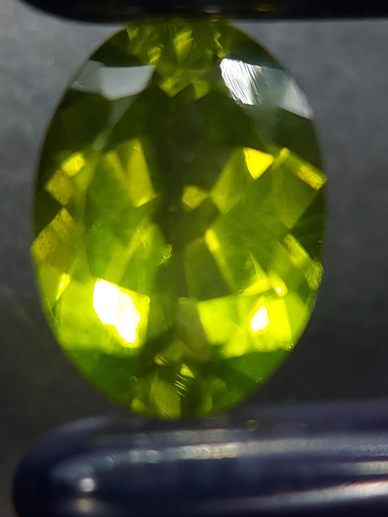 Peut inclure: Une pierre pr&eacute;cieuse ovale de couleur vert vif avec une taille facet&eacute;e. La pierre pr&eacute;cieuse r&eacute;fl&eacute;chit la lumi&egrave;re, montrant sa brillance.