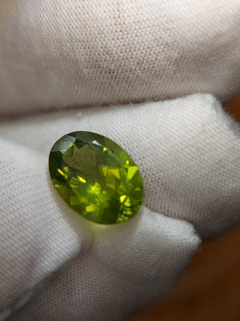 Peut inclure: Une pierre pr&eacute;cieuse ovale de couleur verte avec une taille facet&eacute;e. La pierre est translucide et a une l&eacute;g&egrave;re teinte jaune.